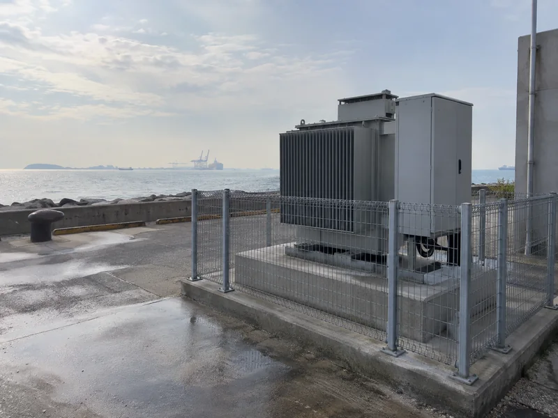 Fenced transformer equipment on a raised concrete pad in a coastal service yard