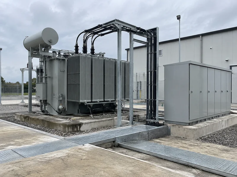 Grey transformer and enclosed switchgear on concrete foundations in an industrial substation yard
